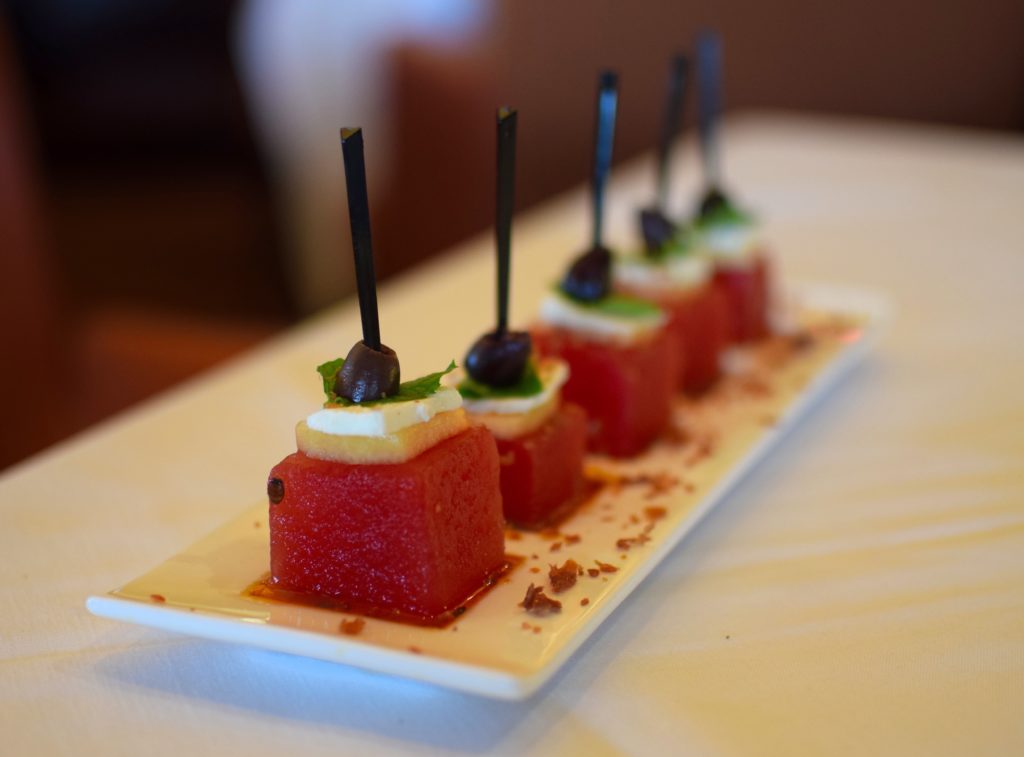 Refreshing summer melon skewers with compressed watermelon, cantaloupe, feta, kalamata olives, chili oil and mint syrup sprinkled with crispy prosciutto.